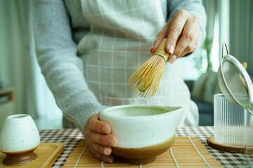 Hands whisking vibrant green matcha tea in a ceramic bowl for a calming ritual.