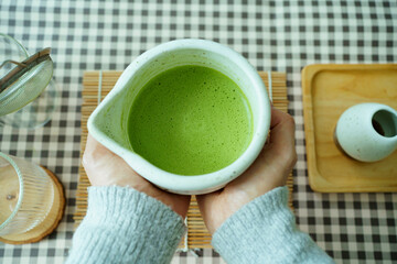 Hands holding ceramic cup of matcha green tea, creating calm and relaxing mood.