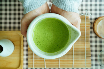 Hands holding ceramic cup of matcha green tea, creating calm and relaxing mood.