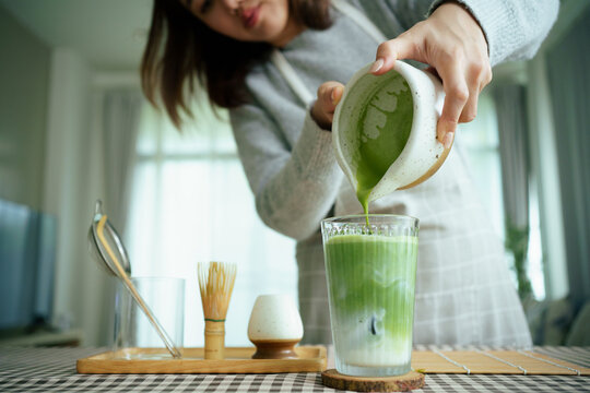 Barista pouring matcha into iced milk to make a layered matcha latte.