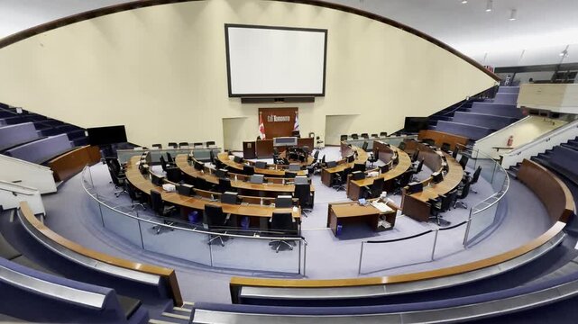 An elevated interior wide shot of the iconic, unoccupied Toronto City Council Chamber in City Hall. The public gallery seating is visible above the council floor