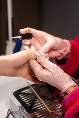 Nail salon. Beauty care. Professional female manicurist hands in pink latex gloves drawing with thin brush acrylic manicure process.