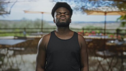 Young man with bare shoulders and closed eyes squinting on a restaurant terrace, facing forward with arms relaxed; relief. - Powered by Adobe