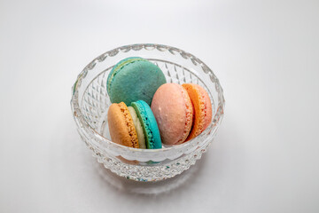 Macro studio shot of pink and blue green sweet macaron cookies in a crystal bowl, on white background with copy space