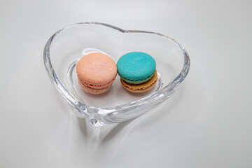 Macro studio shot of pink and blue green sweet macaron cookies in a crystal bowl, on white background with copy space