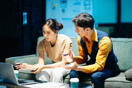Asian couple working together with a tablet and laptop, discussing ideas with smiles. Concept of teamwork