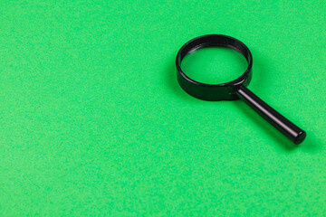 Black magnifying glass on bright green background for clarity and focus
