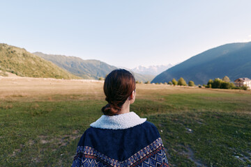Fototapeta premium Woman back overlooking mountain landscape and meadow in a valley, outdoors travel scene with calm nature, rural field and distant hills for peaceful exploration and adventure.