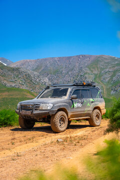 Talas, Kazakhstan - May 13, 2024: A dusty Toyota Land Cruiser 100 with Nitro Energy branding is parked on a sunny dirt road, with green hills and mountains in the background