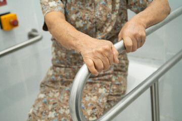 Asian elderly woman patient use toilet support rail in bathroom.