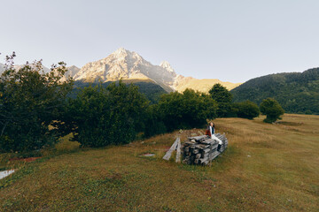 Fototapeta premium Mountain meadow couple standing on stone ruins in a scenic landscape, nature and outdoors travel scene with trees, grassy field and distant peak, romantic hiking moment.