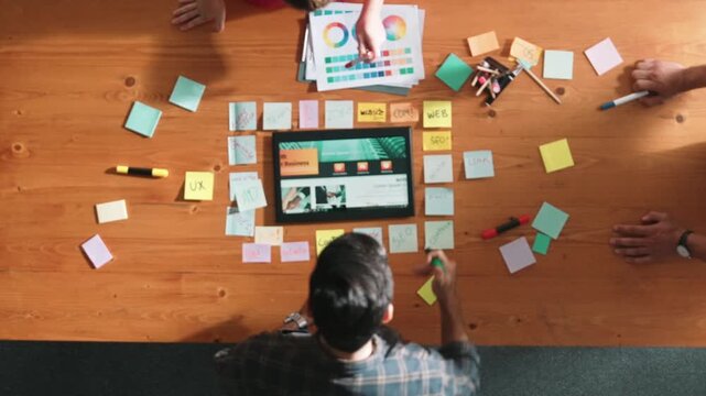 Top view of business people working together to design web design. Aerial view of designer brainstorming and discussing about website interface and looking at tablet with digital design. Symposium.