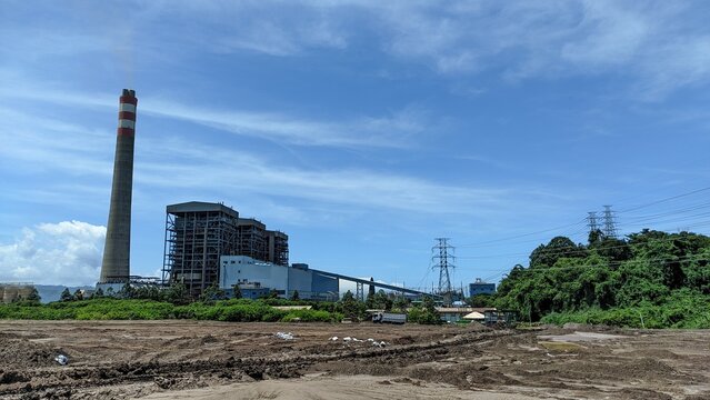 Industrial landscape featuring power plant with towering chimney against bright blue sky generating energy and fuel for cities and homes