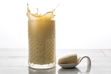 Refreshing banana milkshake splashing in a textured glass, offering a delicious and healthy drink option with fresh fruit