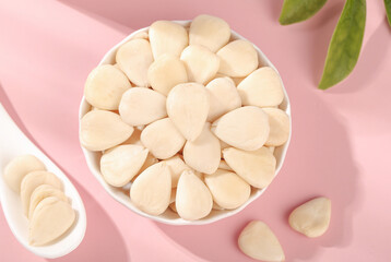 Peeled Blanched Almonds in Bowl on Pink Background with Green Leaves
