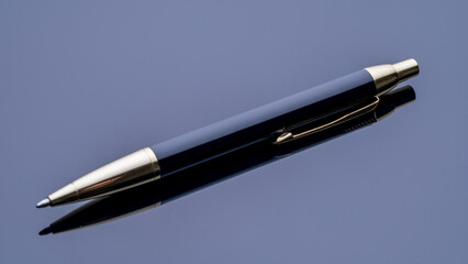 A pen is sitting on a table. The pen is black and has a silver tip. The pen is reflecting the light, creating a shiny and elegant appearance