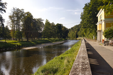 Tranquil river scene with lush green trees, a calm river and charming buildings under a sunny sky, perfect for nature, travel and relaxation themes