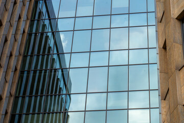 Fototapeta premium A large building with a lot of windows and a cloudy sky in the background. The windows are clear and reflect the sky