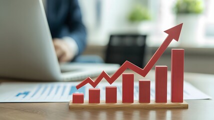 Red upward trending bar graph with arrow indicating financial growth and success on a desk with laptop
