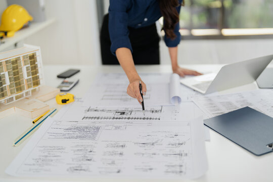 Asian woman engineer designs plans in an office with blueprints - Powered by Adobe