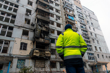 A man looks at the aftermath of a missile strike or artillery shelling of a residential building. Shrapnel marks on the walls and windows shattered by the blast wave.