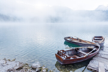 Obraz premium Wooden boats by the pier on a lake at sunset with mist rising over the water