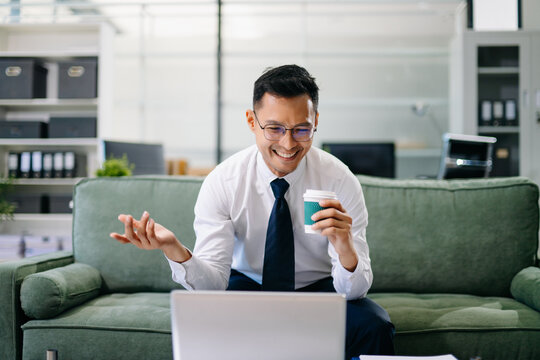 Asian businessman working with a tablet in a modern office, smiling confidently while reviewing documents.