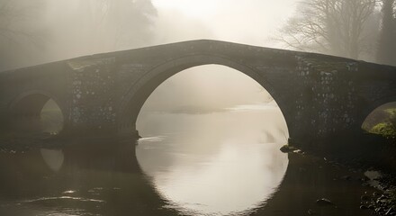 A misty morning view of an old stone bridge over a river with fog rolling in the countryside landscape