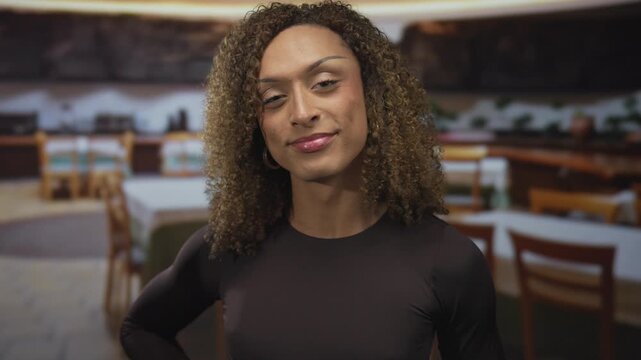 Woman in black shirt smiling while making ok sign with hand in casual restaurant interior; approval calm.