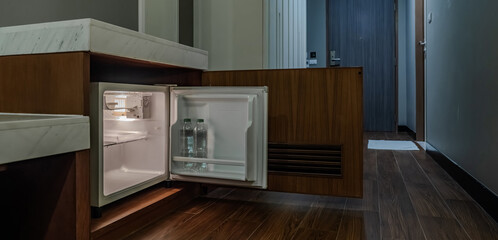 A compact fridge is built under the counter with a wooden door open beside it. The calm room lighting adds a soft tone to the interior setup.