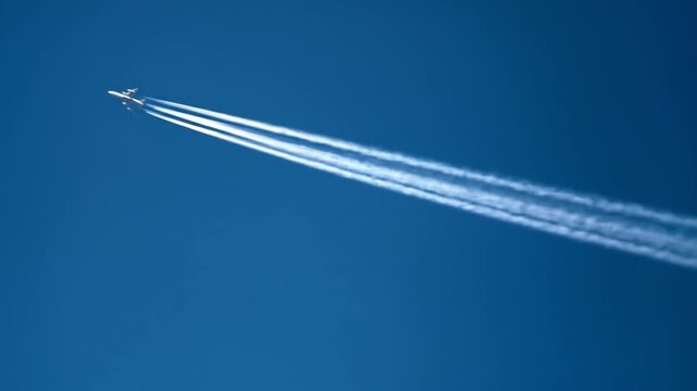 Airplane soaring through clear blue sky leaving condensation trails