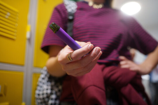 Teen girl holding a vape device in school hallway.