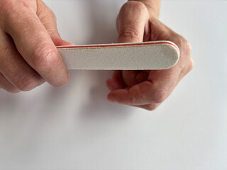 Mature woman filing her nails with a nail file at home, self-care manicure routine, natural nail grooming, beauty and hygiene concept, close-up of female hands during home manicure