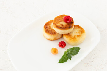 Curd fritters with raspberries on the white plate.
