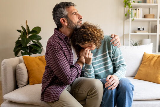 Man comforting crying partner on sofa at home