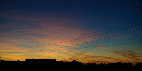 Urban dramatic sunset sky background with picturesque sunset clouds, wires and silhouettes of the...