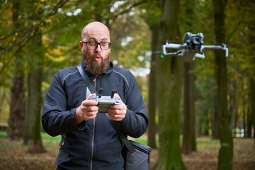 In a colorful forest filled with autumn leaves, a man excitedly operates a drone with a remote. His surprise showcases the thrill of flying technology in nature.
