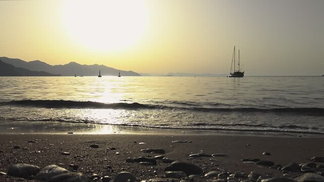 The view of a yacht at anchor and a few sparkling sea ripples during a golden sunrise from the beach at Turunc, Mugla, Turkey