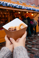 Clous up of hands holding the Christmas churros gingerbread at Christmas Warsaw market with decorated wooden stalls, Christmas trees and festive ornaments.