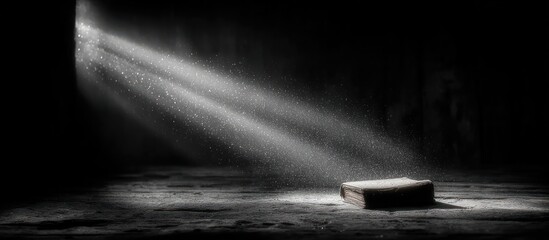 Dramatic light illuminates a book on a weathered surface in a dark space