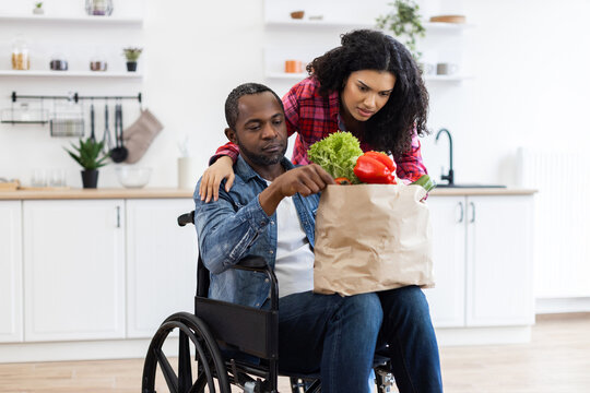 A Black couple in a modern kitchen, one in a wheelchair, unpacking groceries together, promoting inclusivity and healthy eating. - Powered by Adobe