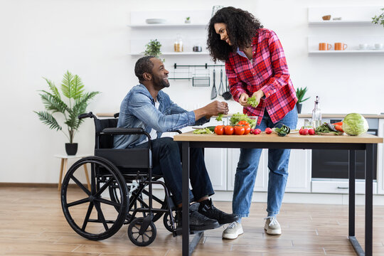 A smiling couple prepares a meal together in a bright, modern kitchen, with one person using a wheelchair.
