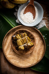 A beautifully arranged set of traditional Thai sticky rice desserts wrapped in banana leaves and tied with natural fibers, presented in a rustic bamboo basket. The scene features warm, cultural tones 