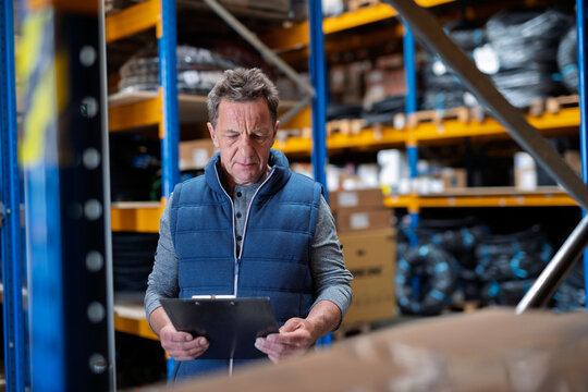 Older warehouse worker working looking at document in clipboard. - Powered by Adobe