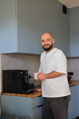 Smiling man making coffee with an espresso machine in a bright modern kitchen at home