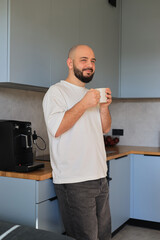 Smiling man standing in the kitchen with a cup of coffee, enjoying a relaxed morning moment at home