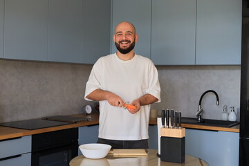 Smiling man preparing carrots in a modern kitchen, enjoying a relaxed cooking moment during everyday home life