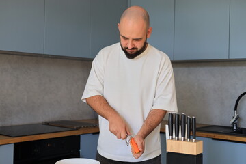 Man concentrating while cutting carrots in the kitchen, carefully preparing vegetables during a focused home cooking routine