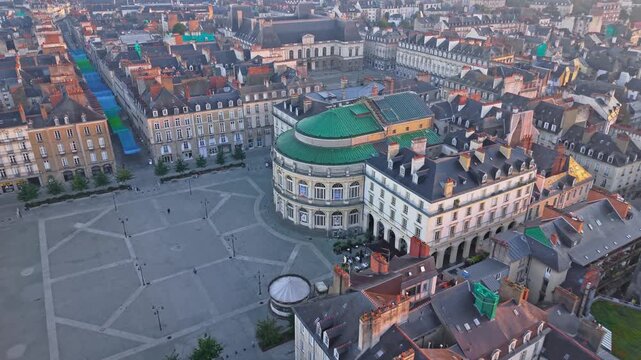 Drone advancing over Place de la Mairie toward Rennes Opera with the Parlement de Bretagne visible in the background in Rennes, France at sunrise.