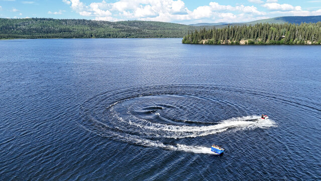 Thrilling water sports adventure with jet ski and tubing on stunning blue lake surrounded by vibrant green forest in Alaska, perfect for summer vacation promotions